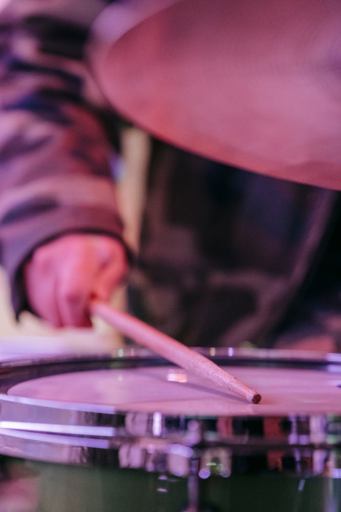 A drummer's hand strikes a snare drum with a stick during a vibrant concert performance.