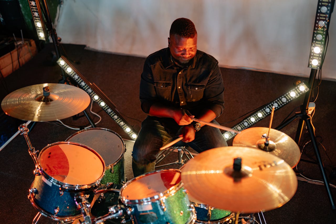 A passionate drummer playing in a dimly lit studio with vibrant lighting and a modern drum set.